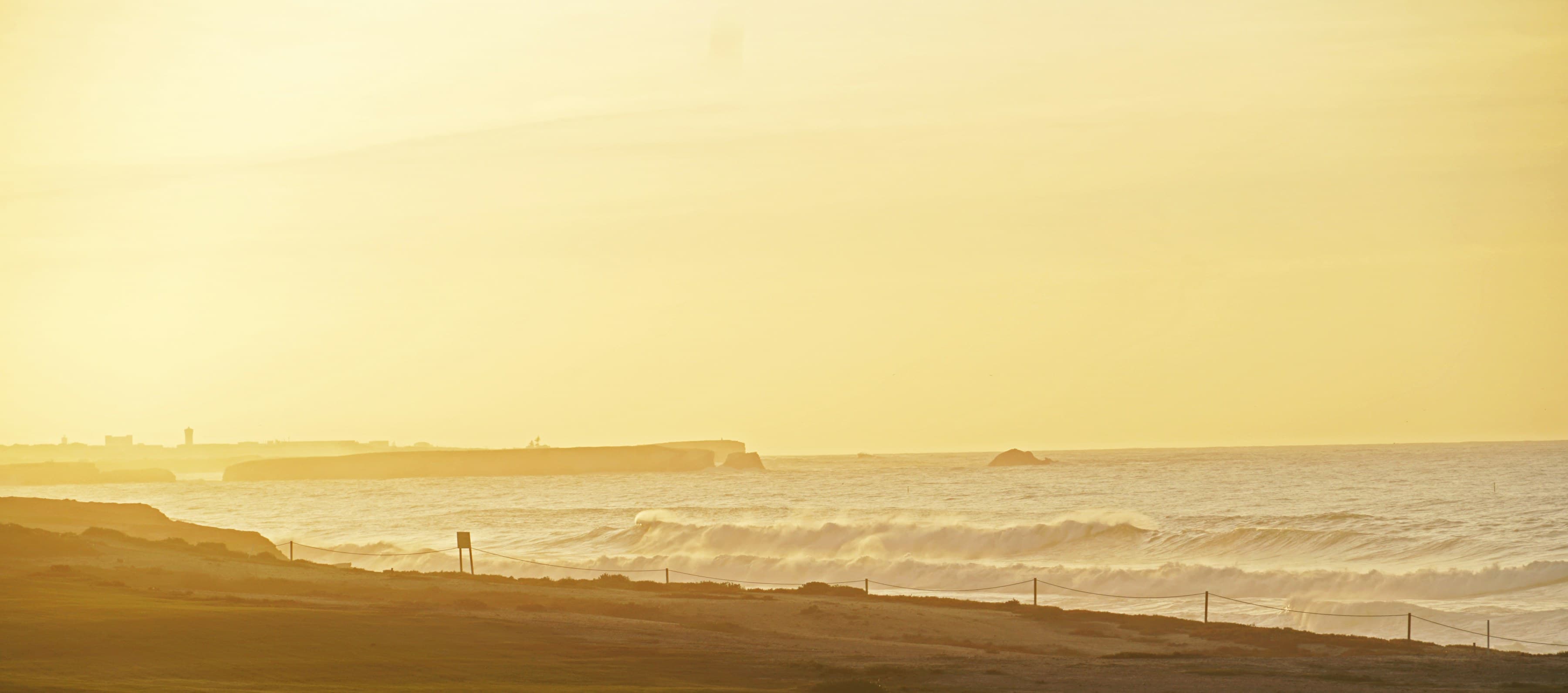 Golden-hour view of Praia D'el Rey golf links in Portugal, with waves breaking along the coastline